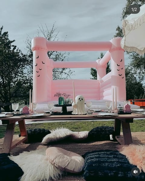 Pink inflatable bounce house with ghost decorations and seating area in foreground at outdoor event