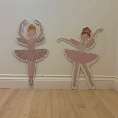 Two pink decorative ballerina wall cutouts in different poses mounted on a white wall above wooden flooring