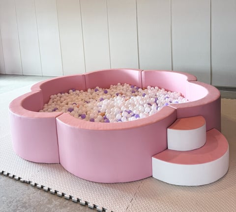 Pink and white foam ball pit with pink and white foam balls, steps, and white foam tiles in a playroom