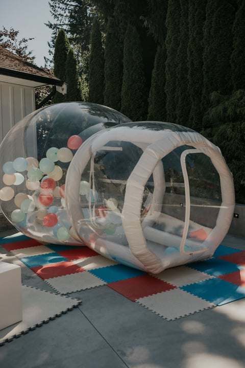 Clear inflatable play tunnel for children filled with colorful balls, set up on a colorful foam mat in a driveway