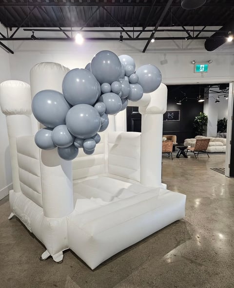 White inflatable bounce house decorated with gray and white balloons in an indoor event space
