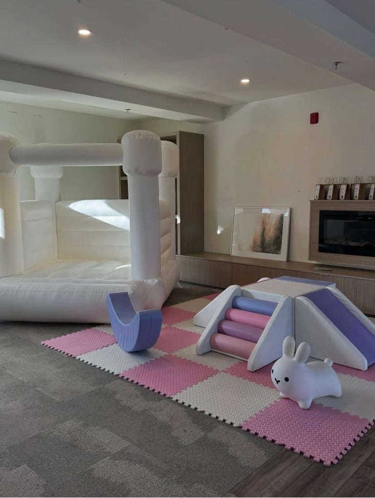 Modern playroom with white inflatable bounce house, pink foam play mats, climbing structure, and white bunny toy on cushioned floor