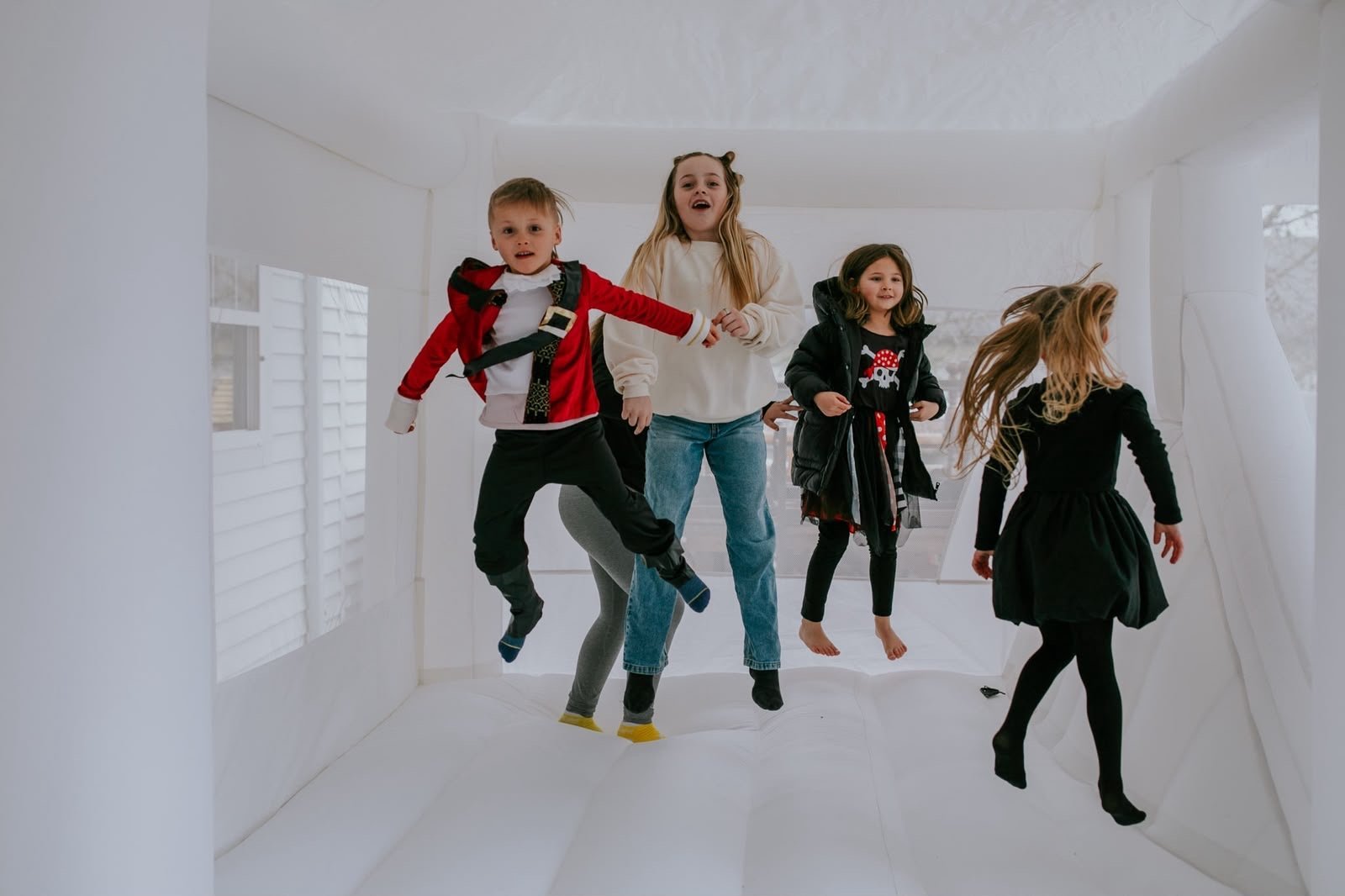 Five children jumping and playing together in a bright, white empty room