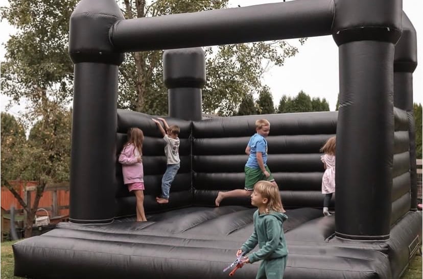 Children playing in a large black inflatable bounce house with trees visible in the background
