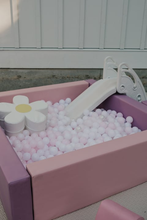 Pink ball pit with white plastic balls, a white flower toy, and toy containers inside