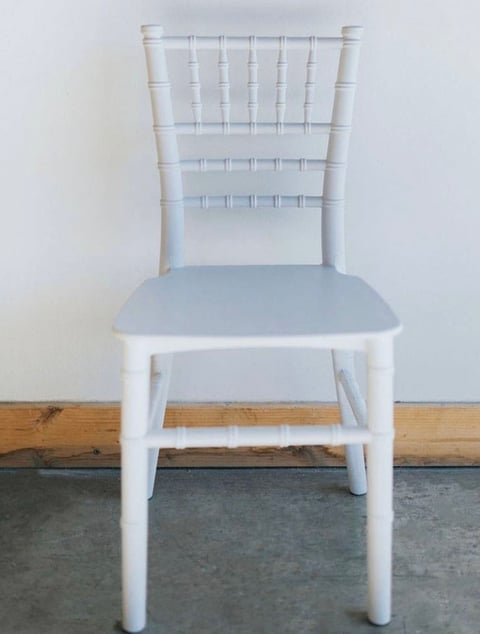 White Chiavari chair with light blue cushion seat against white wall and wooden baseboard