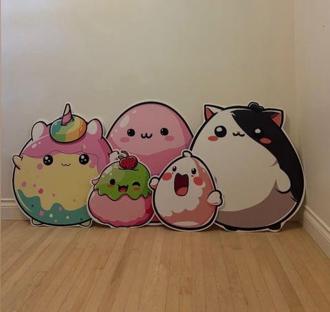 Collection of five plush kawaii character toys lined up on a wooden floor against a white wall, featuring cute pastel-colored designs