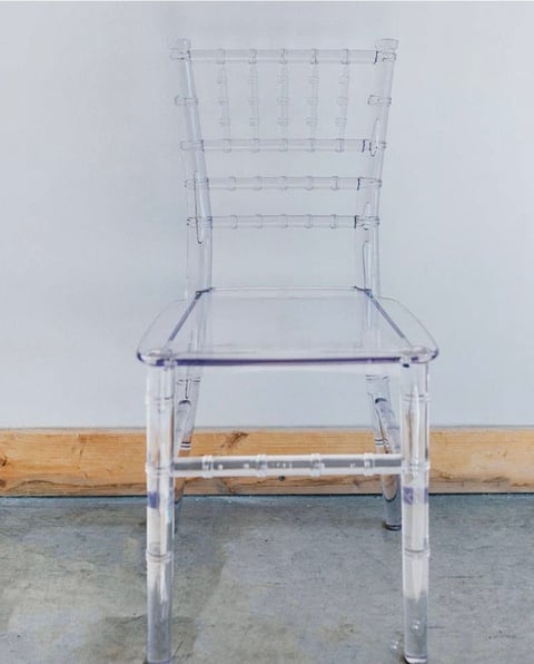 Clear transparent modern chair with gridded back positioned against a wall with wooden and concrete surfaces