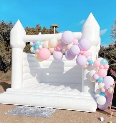 White inflatable bounce house with pink and purple balloon garland decoration in outdoor setting