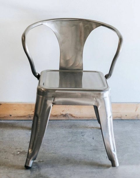 Polished metal industrial-style chair with curved backrest and armrests on concrete floor