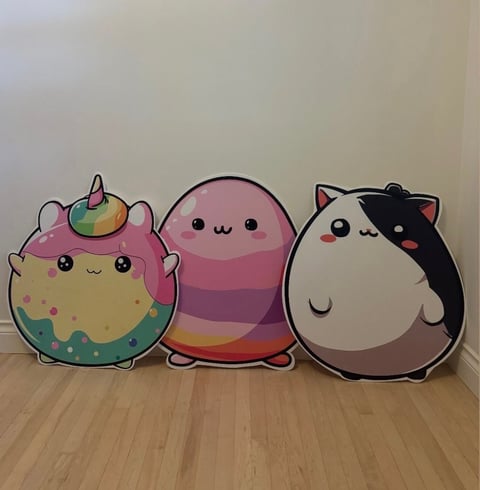 Three plush toys lined up on a wooden floor: a pink unicorn, a rainbow-striped jellyfish, and a black and white cat