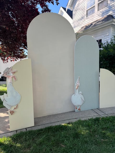 Whimsical outdoor art installation with arched white structure and decorative duck panels in front of white house